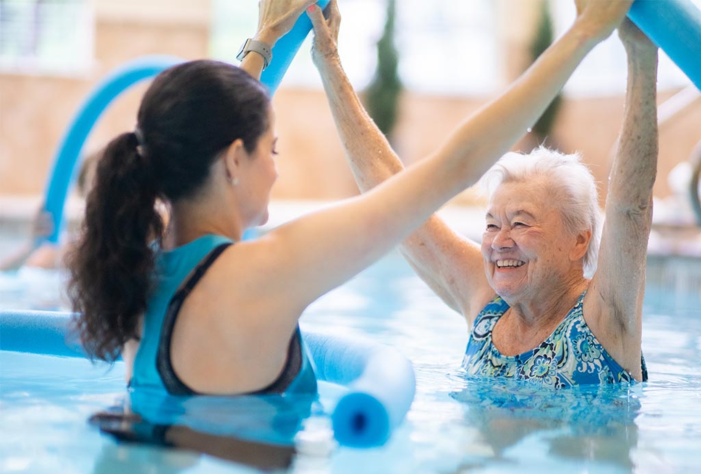 A smiling senior woman participating in a water aerobics class with an instructor at a Franklin Park Senior Living community.