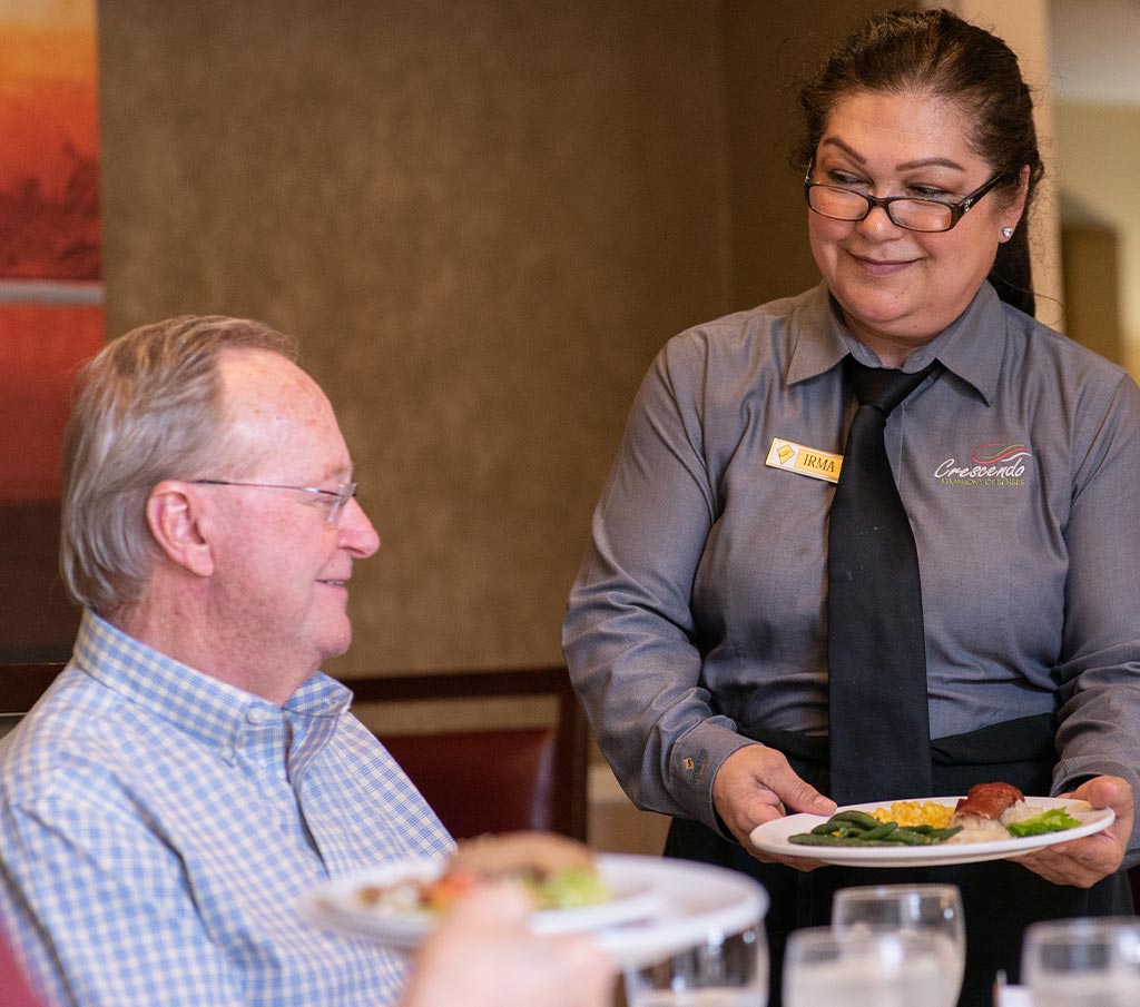 Franklin Park Senior Living team member speaking with an older adult in a community dining area.