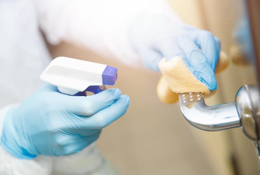 Staff member wearing protective gloves disinfecting a door handle at a Franklin Park Senior Living community.